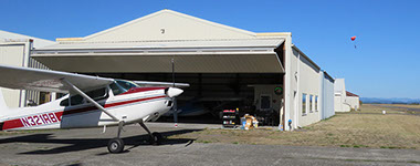 A small aircraft is parked in front of a hangar at the airport.